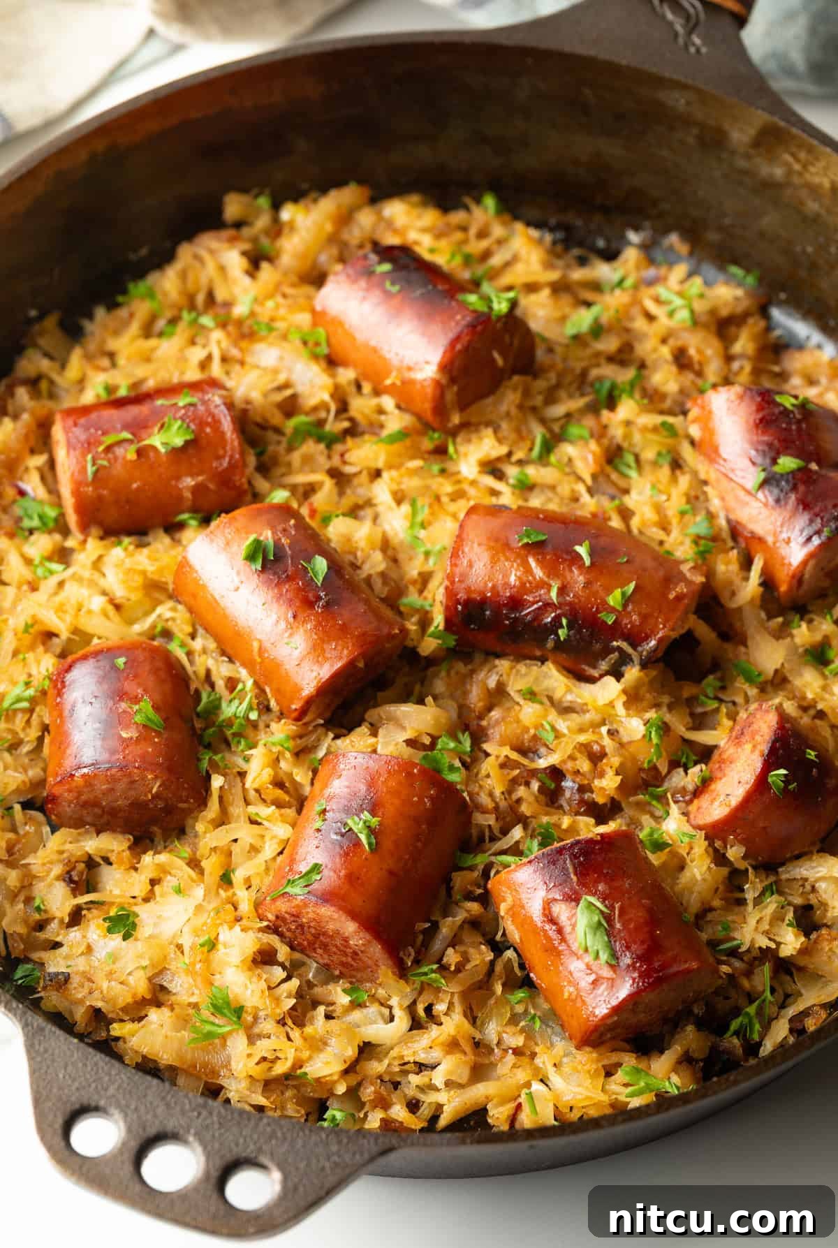 Large skillet with browned sauerkraut and 8 pieces of cooked kielbasa sausage.