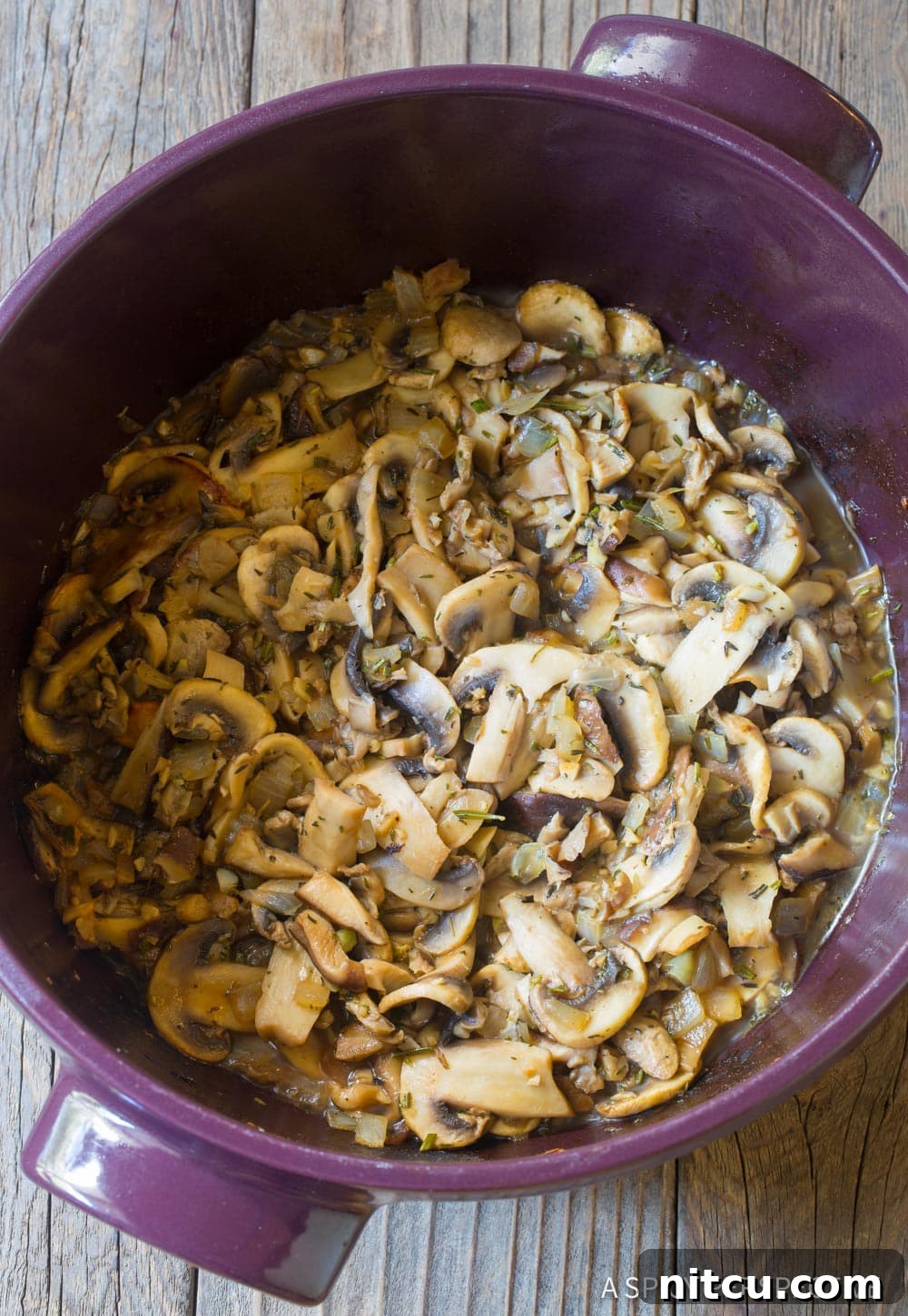 Close-up shot of sliced mushrooms, rosemary, and thyme sautéing in a pot.