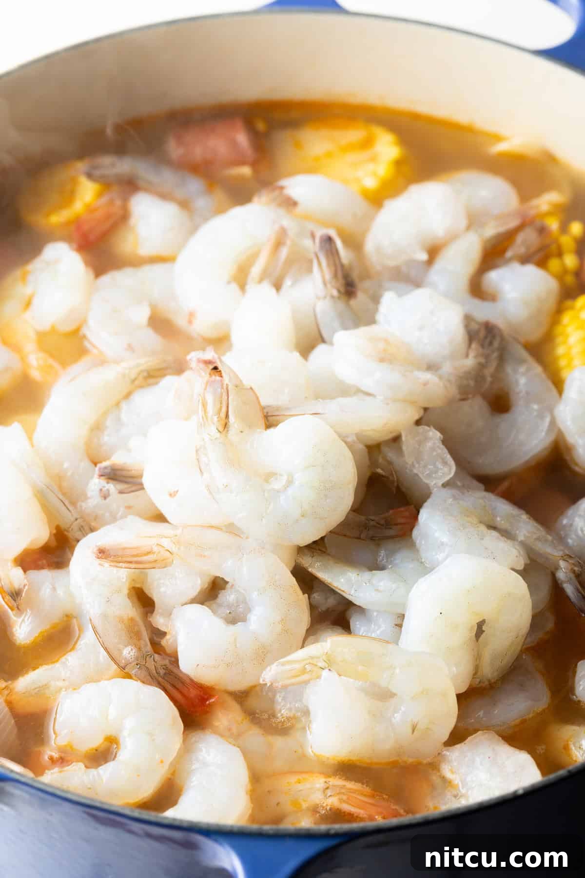 Coastal Bounty Boil 8 Fresh, raw shrimp are being carefully added to the vibrant pot of low country shrimp and sausage boil, ready to cook quickly and absorb the rich flavors.