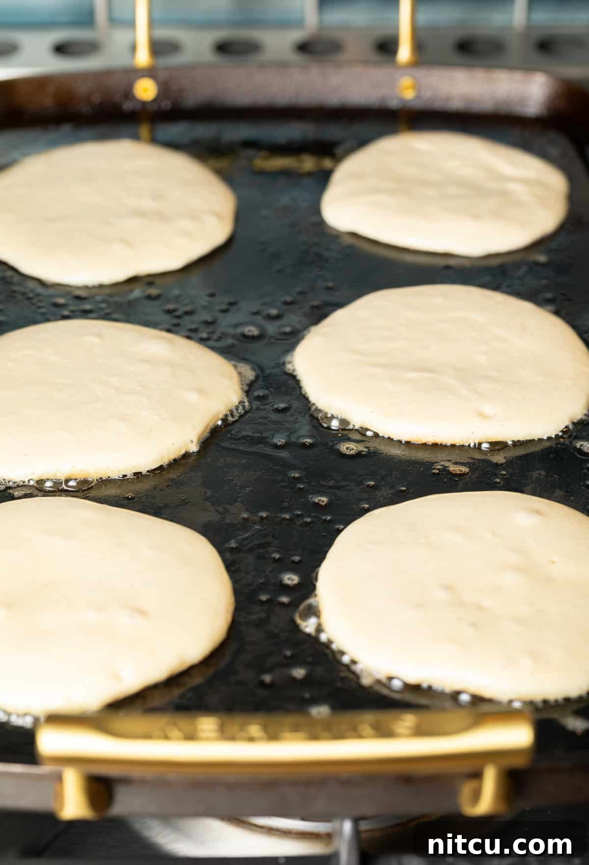 Fluffy homemade pancakes sizzling on a griddle before flipping.