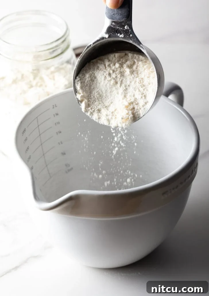 A scoop of homemade pancake mix is being poured into a mixing bowl.
