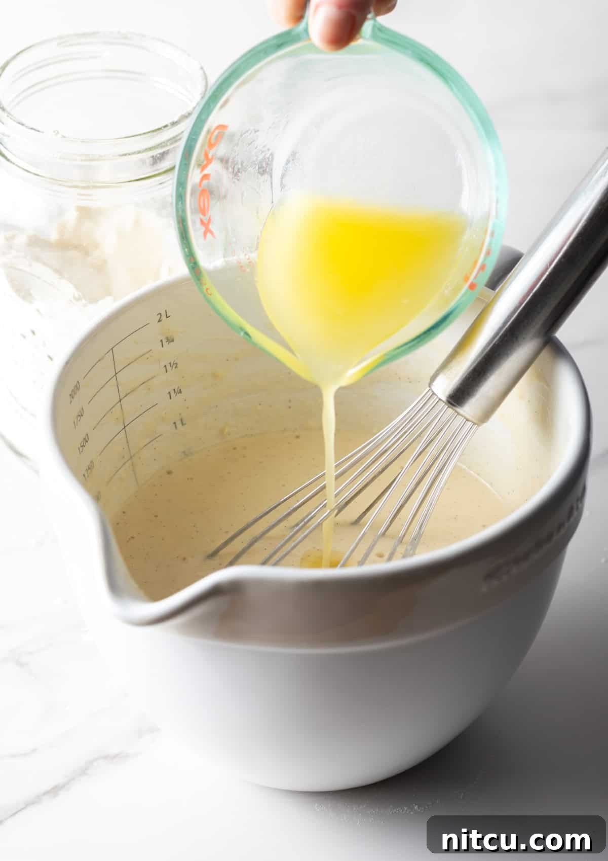 Melted butter is being added to a mixing bowl filled with a homemade pancake mix recipe.
