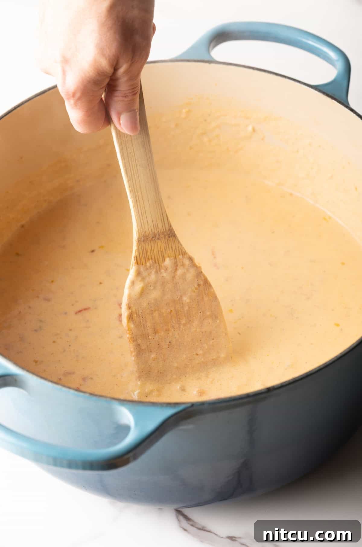 Big Easy Mac and Cheese 7 A wooden spoon is stirring the milk and roux mixture in a pot.