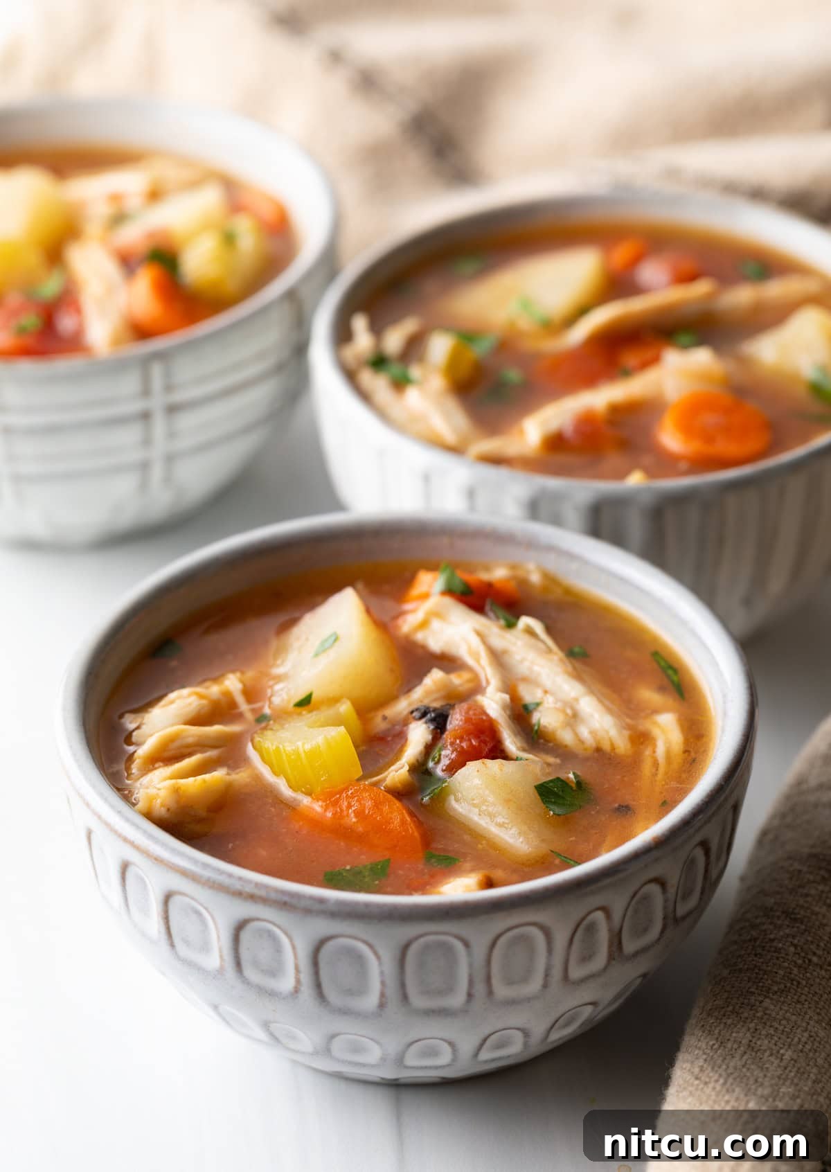 Soul-Satisfying Slow Cooker Chicken Stew 2 3 small white bowls of chicken stew with potatoes, carrots, and celery in a tomato broth.