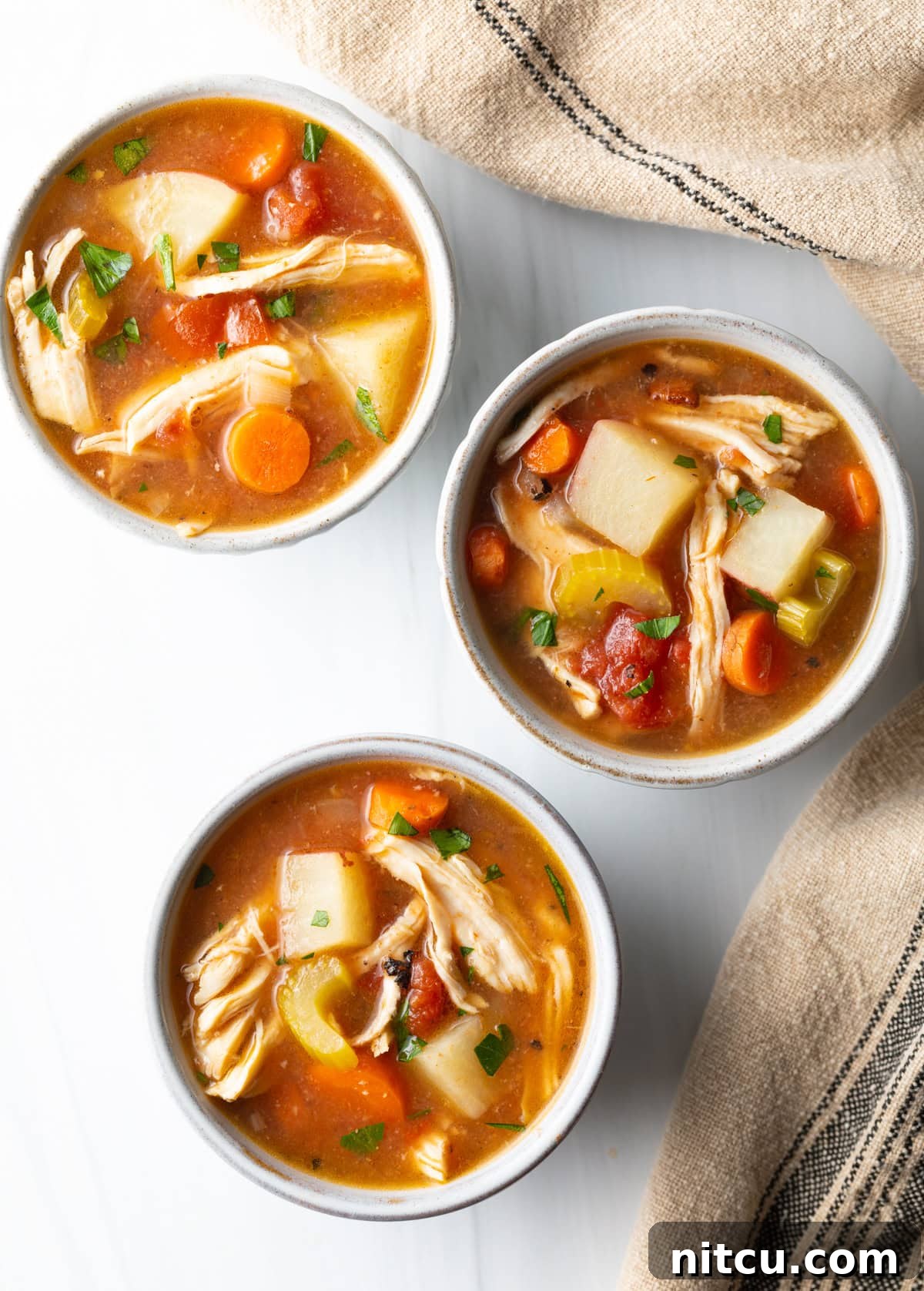 Soul-Satisfying Slow Cooker Chicken Stew 12 Top down view of 3 small white bowls of chicken stew with potatoes, carrots, and celery in a tomato broth.