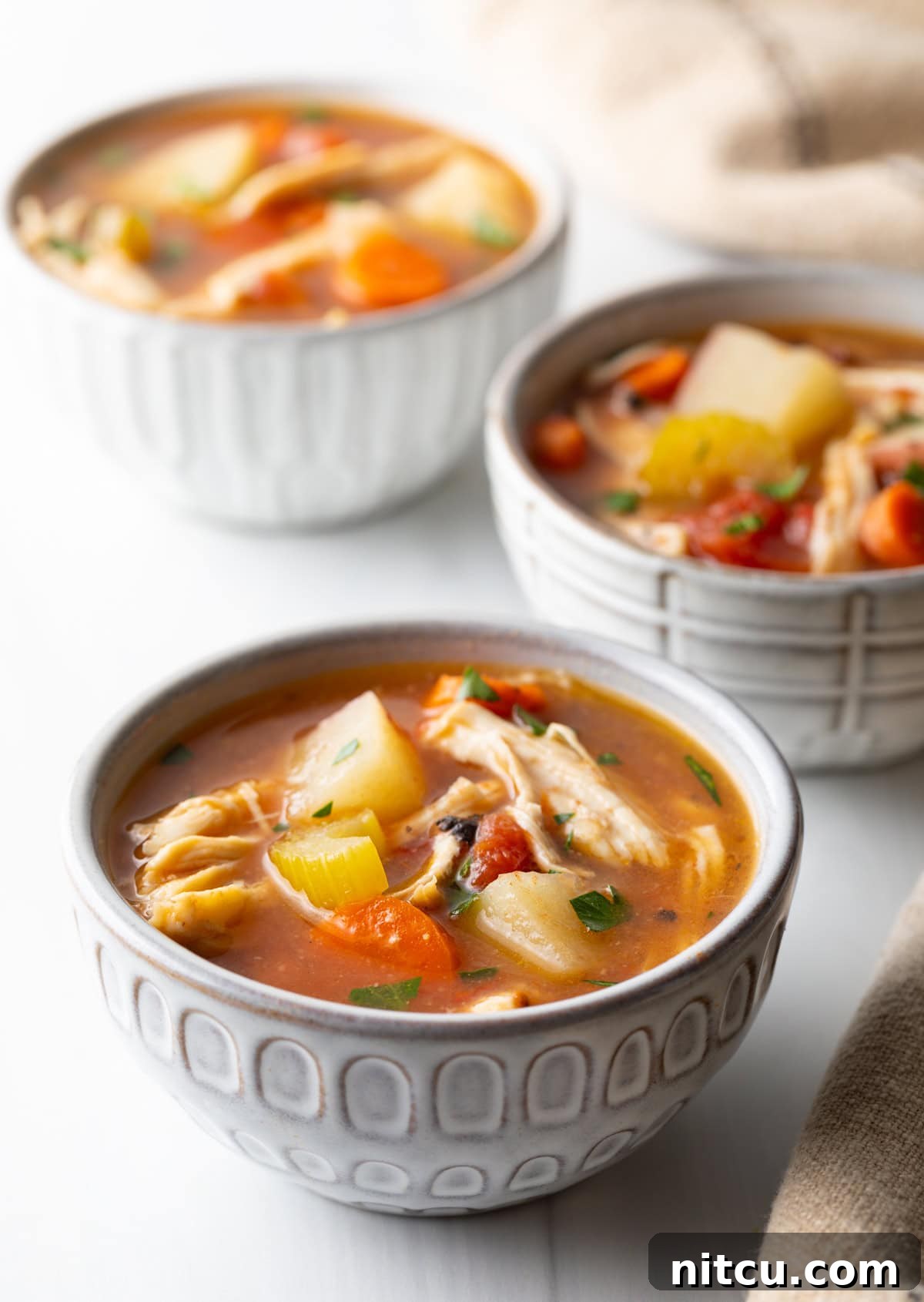 Soul-Satisfying Slow Cooker Chicken Stew 13 3 small white bowls of chicken stew with potatoes, carrots, and celery in a tomato broth.