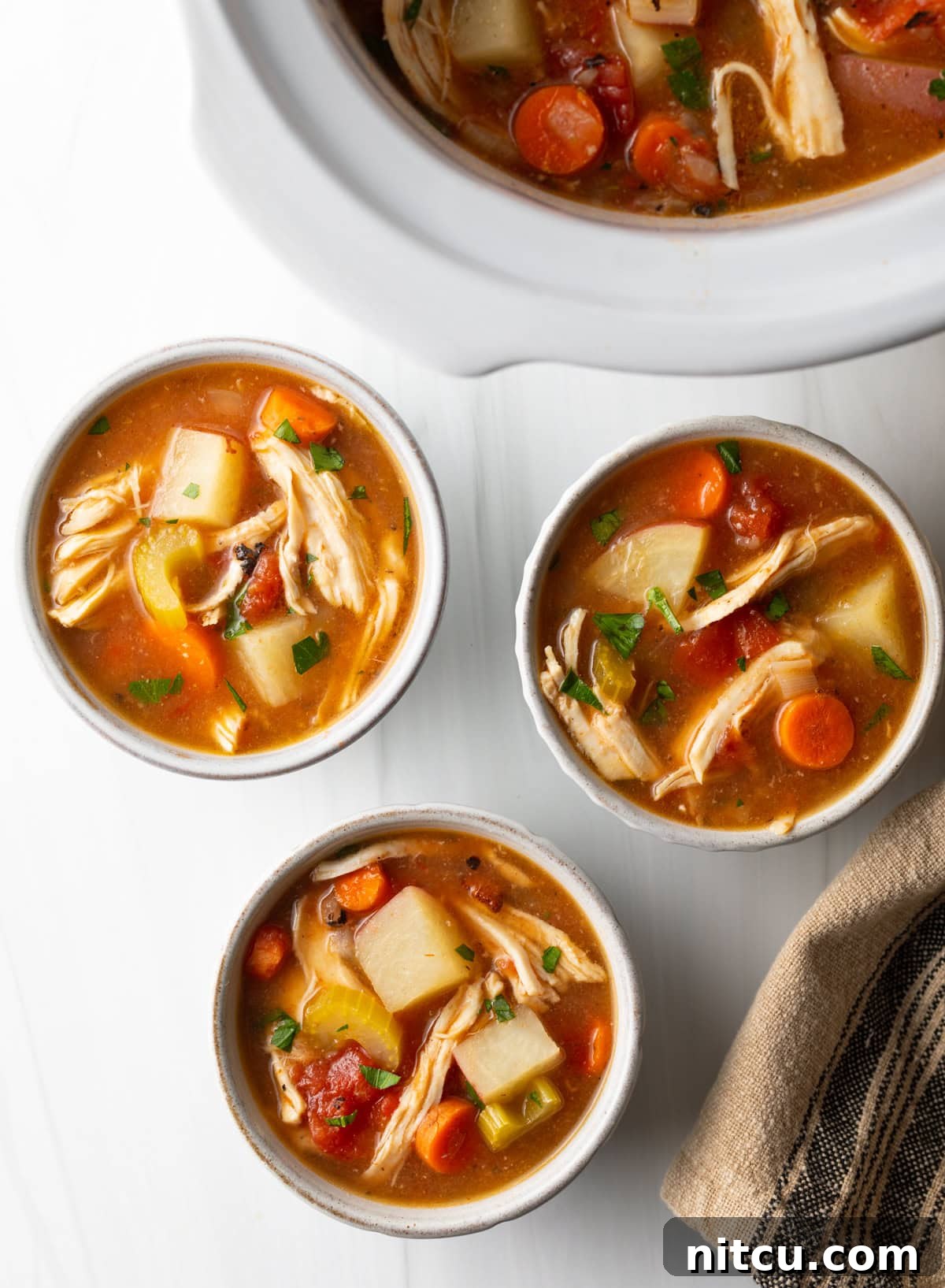 Soul-Satisfying Slow Cooker Chicken Stew 3 Top down view of 3 small white bowls of chicken stew with potatoes, carrots, and celery in a tomato broth.