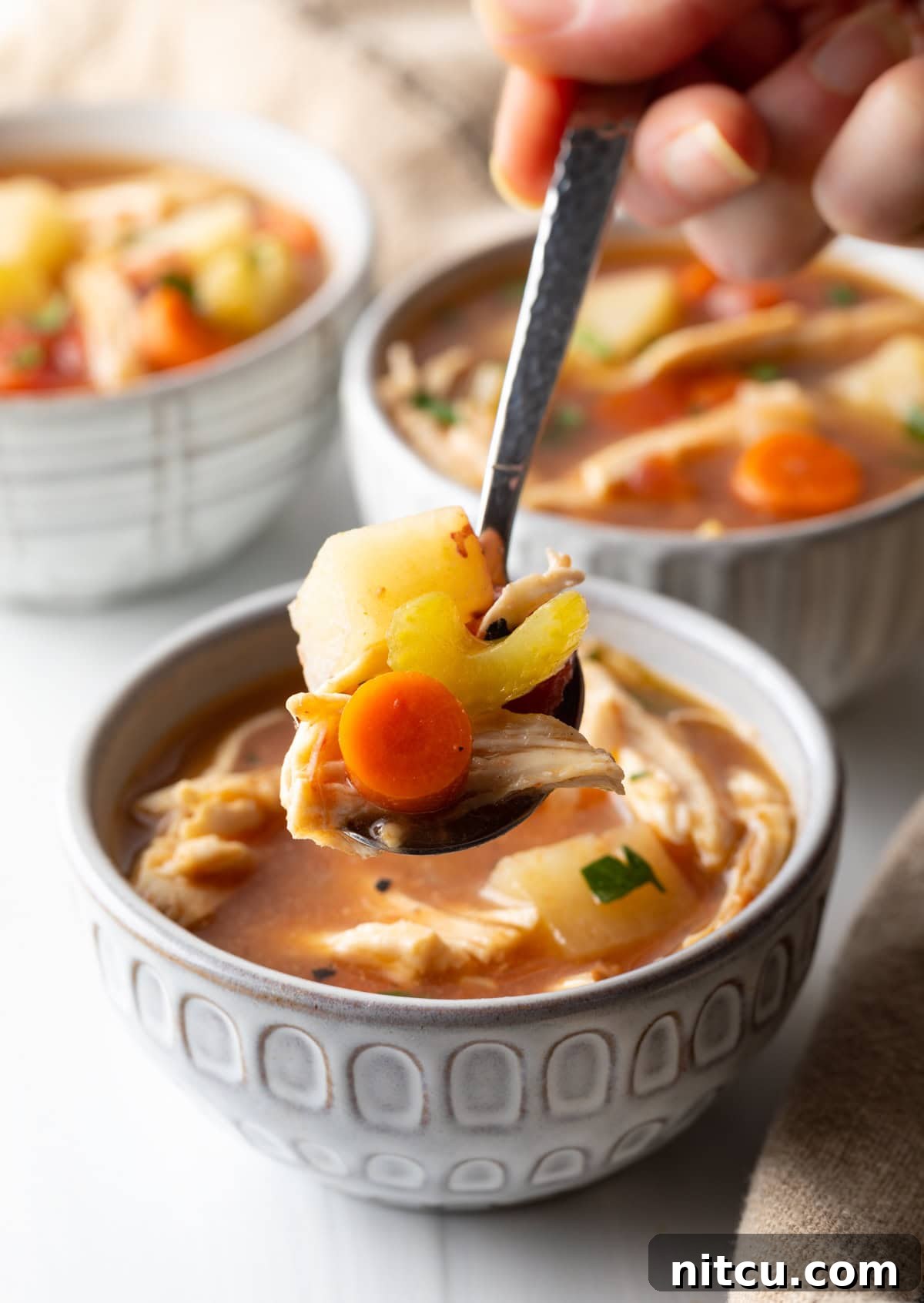 Soul-Satisfying Slow Cooker Chicken Stew 5 Hand holding a spoonful of tomato, chicken, carrot and potato soup to camera.