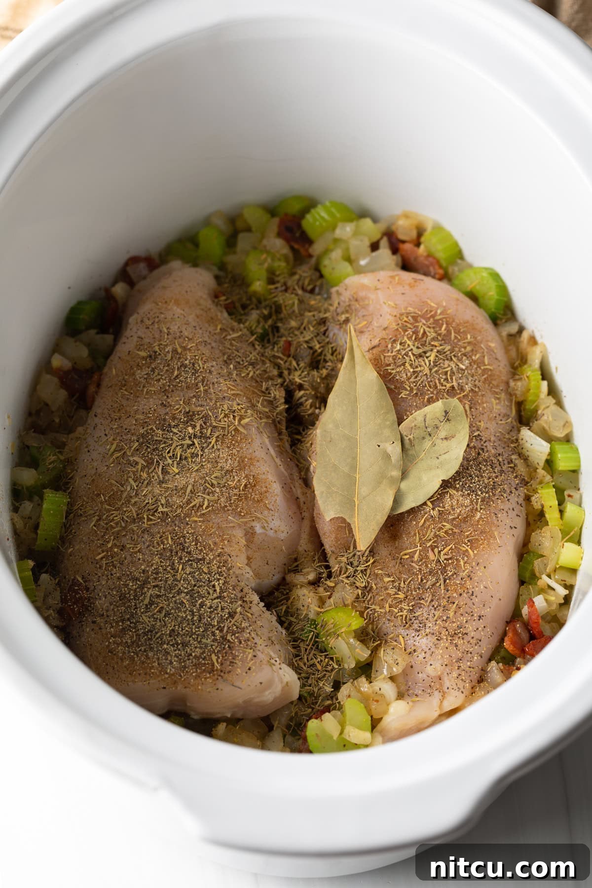 Soul-Satisfying Slow Cooker Chicken Stew 7 Two raw seasoned chicken breasts in a white crock pot.