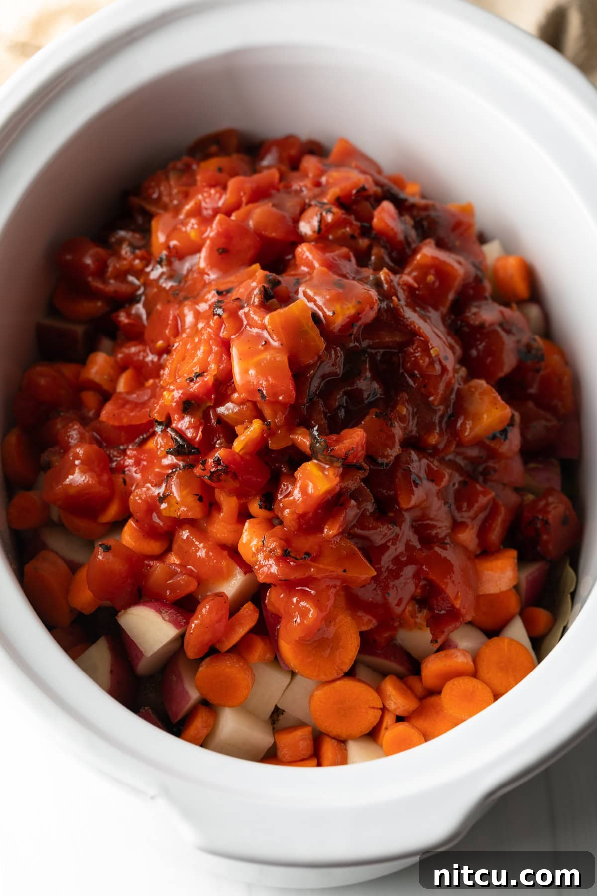 Soul-Satisfying Slow Cooker Chicken Stew 8 Canned diced tomatoes added onto the veggies in a white slow cooker.