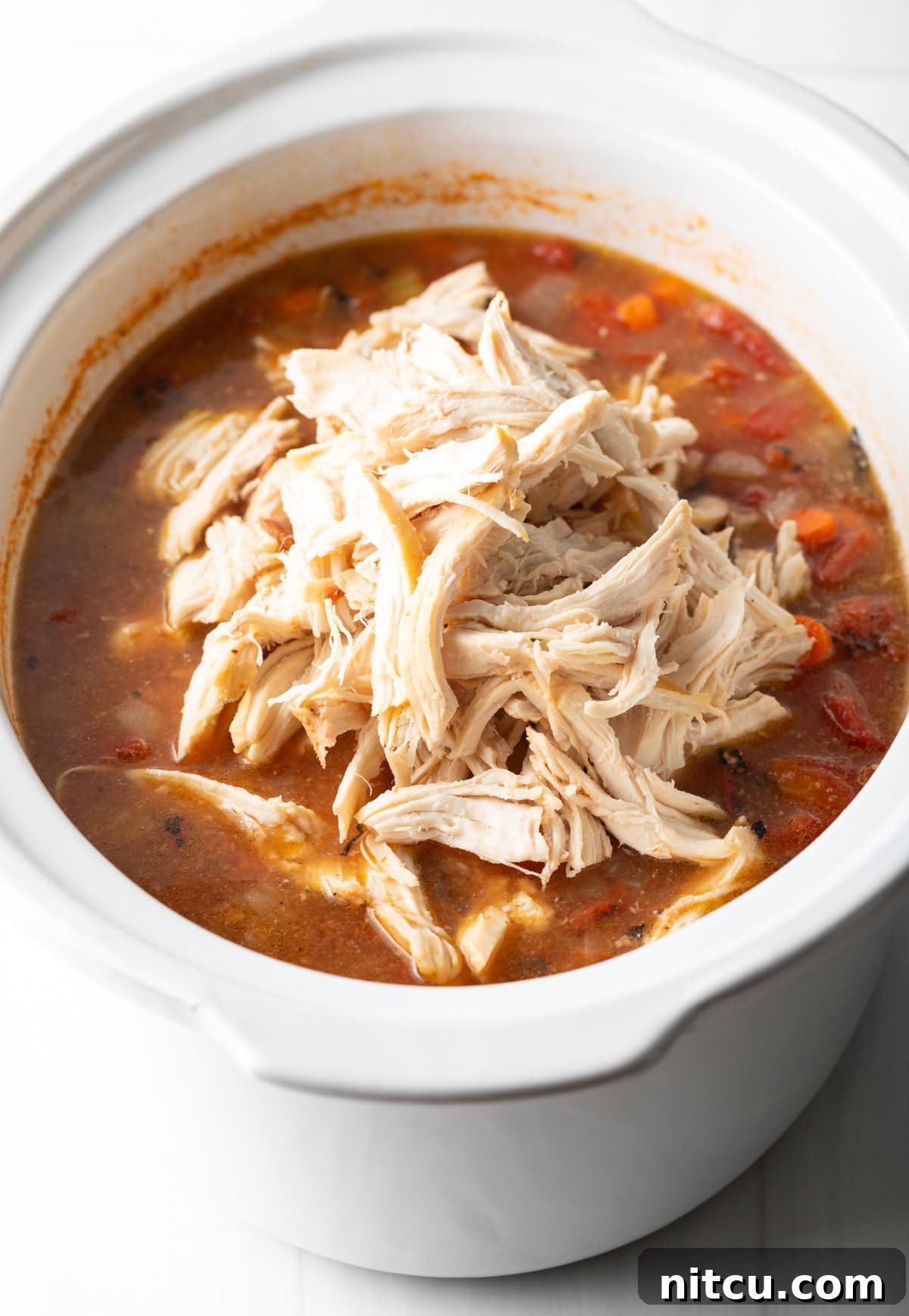 Soul-Satisfying Slow Cooker Chicken Stew 9 Shredded chicken on top of a tomato soup base in a slow cooker.