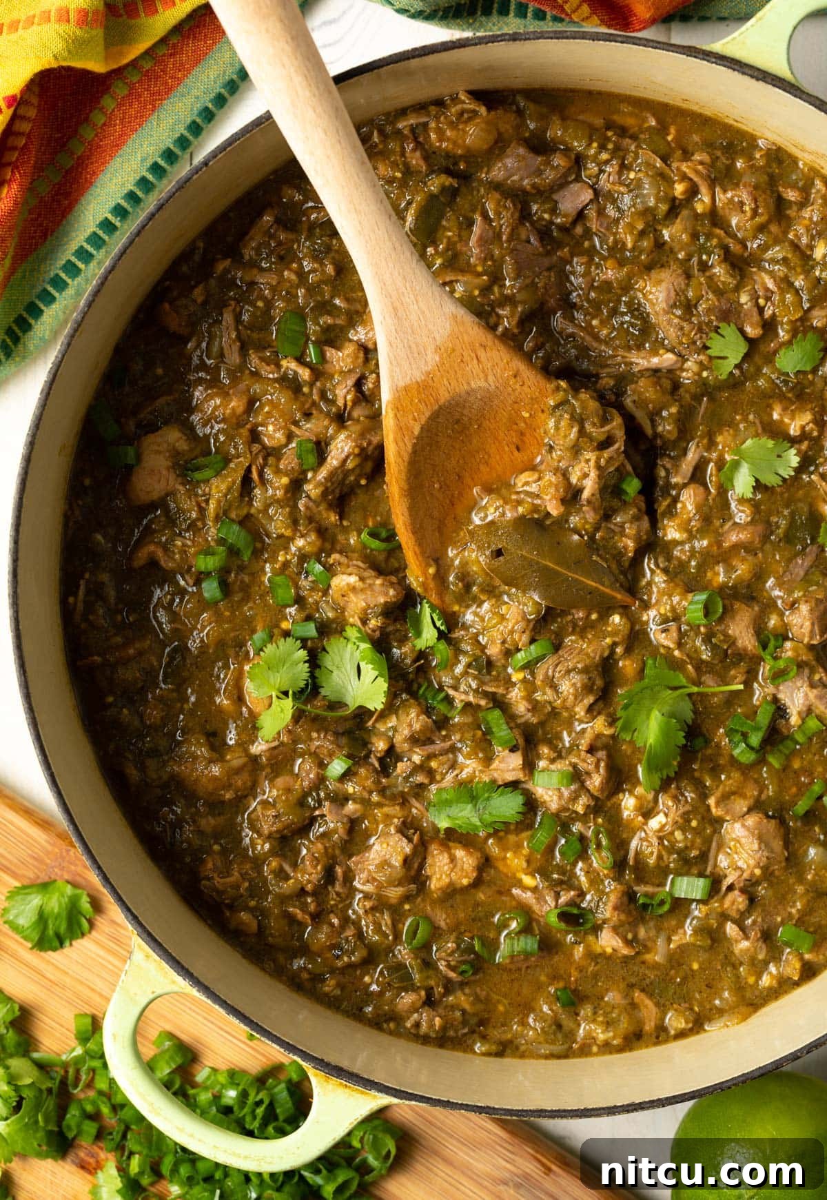 Signature New Mexico Green Chile Stew 2 Dutch oven full of savory pork green chili with a wooden spoon, ready to be served.
