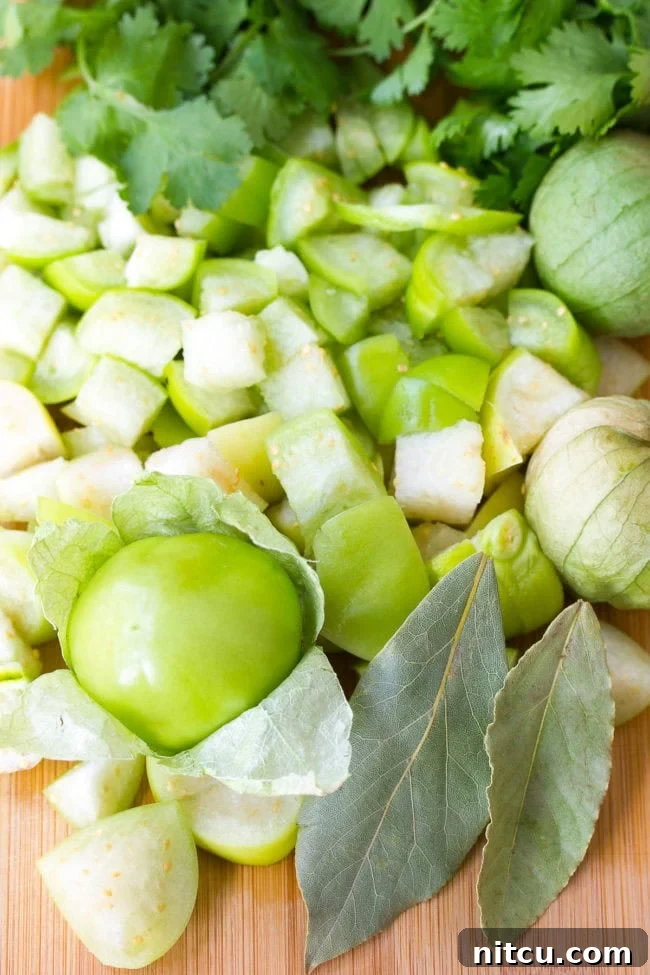 Signature New Mexico Green Chile Stew 5 Diced tomatillos on a cutting board alongside fresh cilantro and bay leaves, prepared for a recipe.