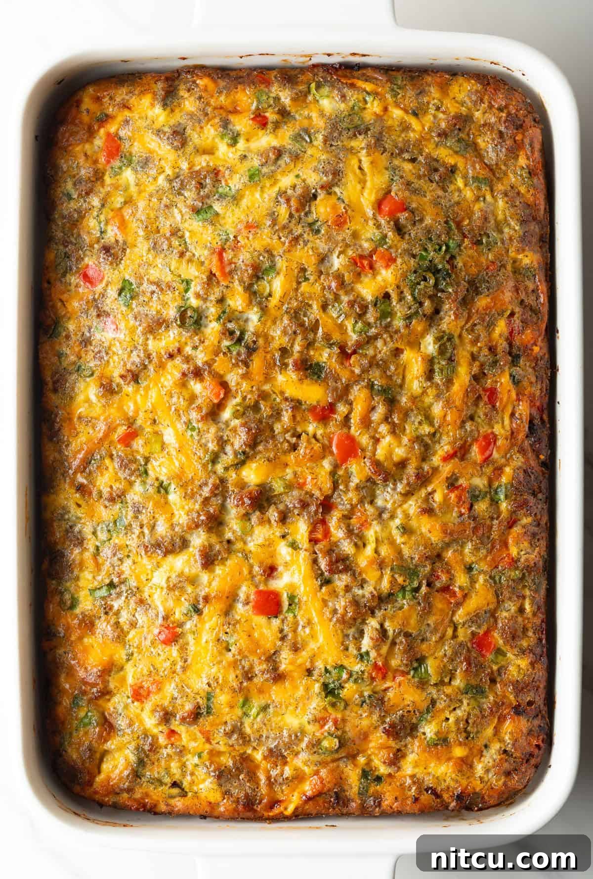 Savory Morning Sausage Bake 11 Top down view of a baked egg, sausage, and cheese casserole in a white rectangle dish.