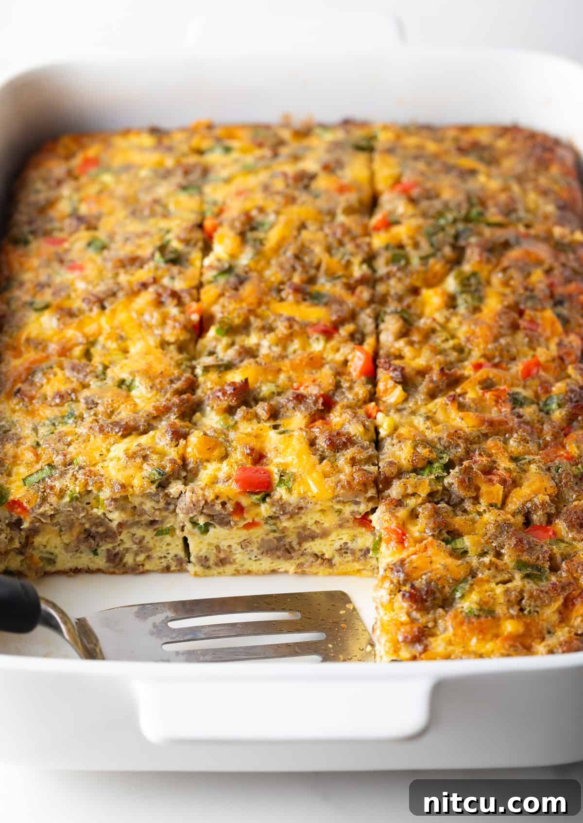 Savory Morning Sausage Bake 12 Pan of egg casserole with sausage and vegetables. A spatula is in the pan, with square portions of the casserole removed.