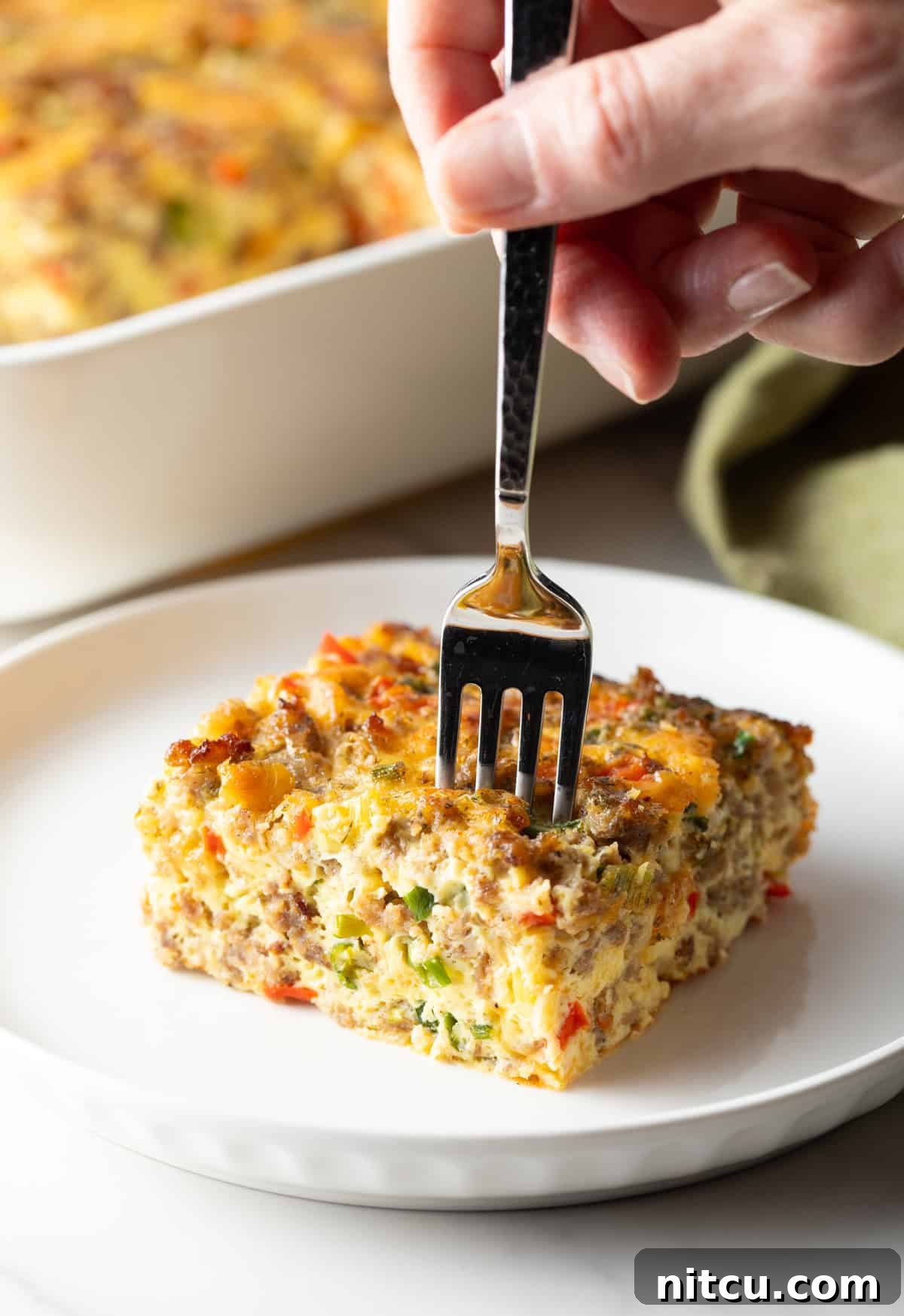 Savory Morning Sausage Bake 13 Fork taking a section from a square of sausage breakfast casserole on a white plate.