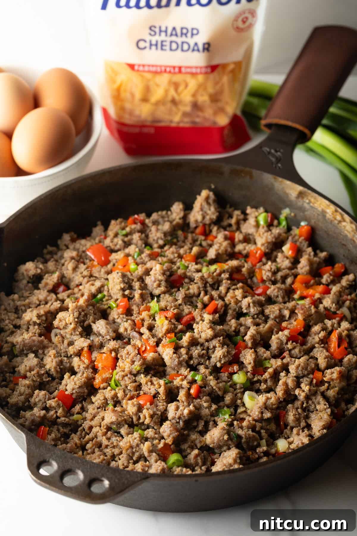 Savory Morning Sausage Bake 6 Cooking ground sausage in a cast iron skillet with diced red peppers.