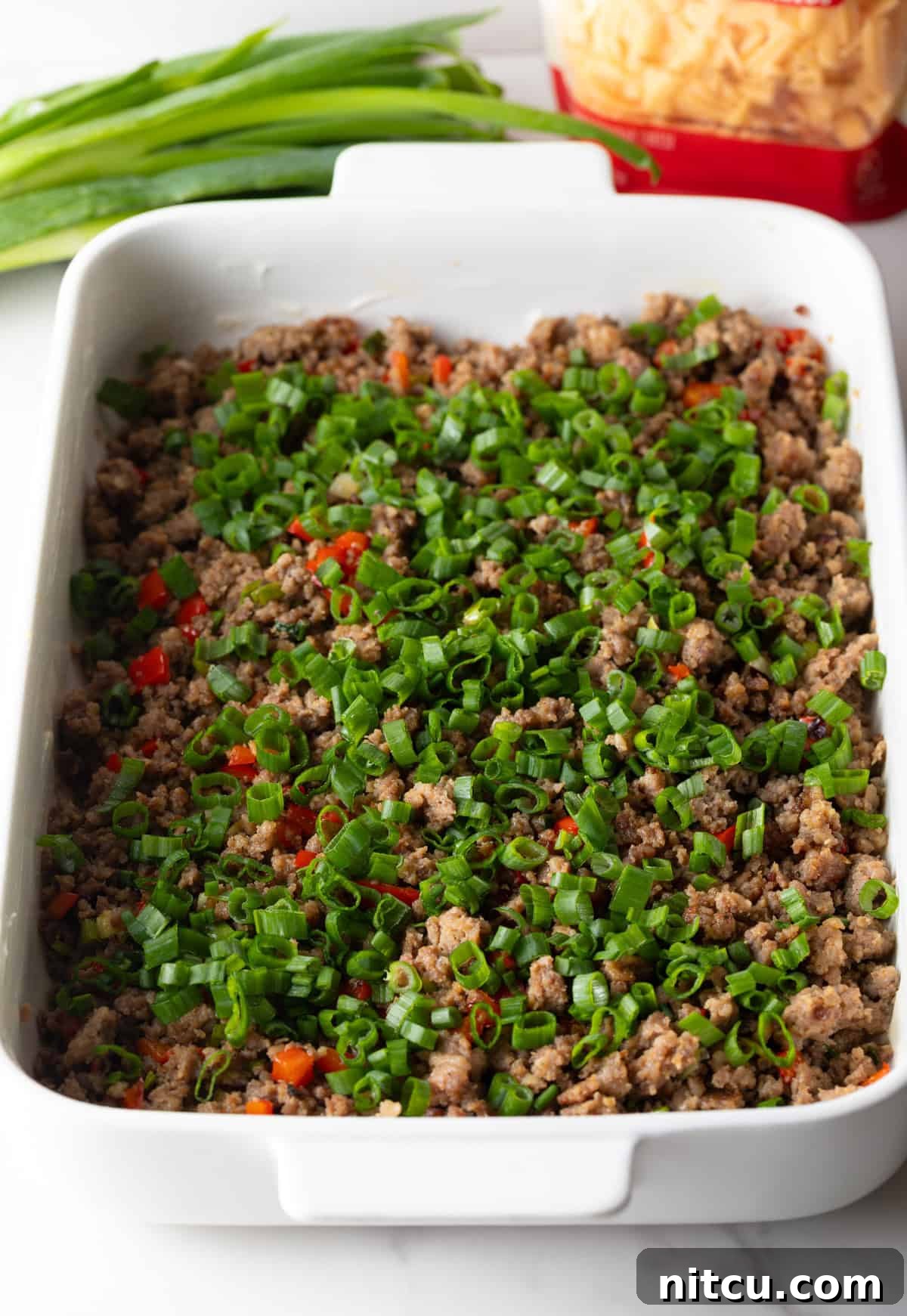 Savory Morning Sausage Bake 7 Cooked sausage and bell pepper mixture spread evenly in a white rectangle baking dish.