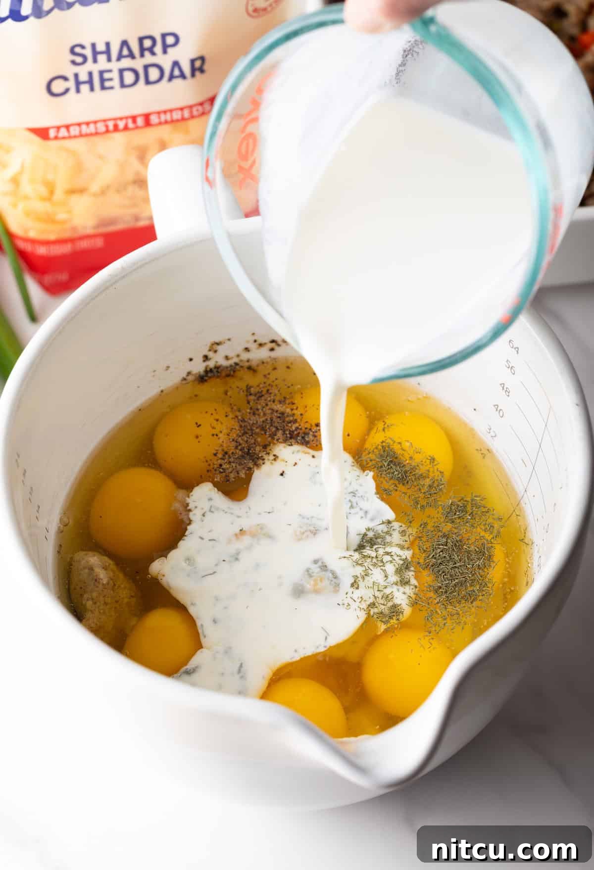 Savory Morning Sausage Bake 8 Adding milk to raw eggs in a white measuring pitcher.