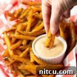 Next-Level Fry Sauces 11 A basket of crispy French fries with a ramekin of French fry dipping sauce, and a hand is dipping two fries into the sauce.