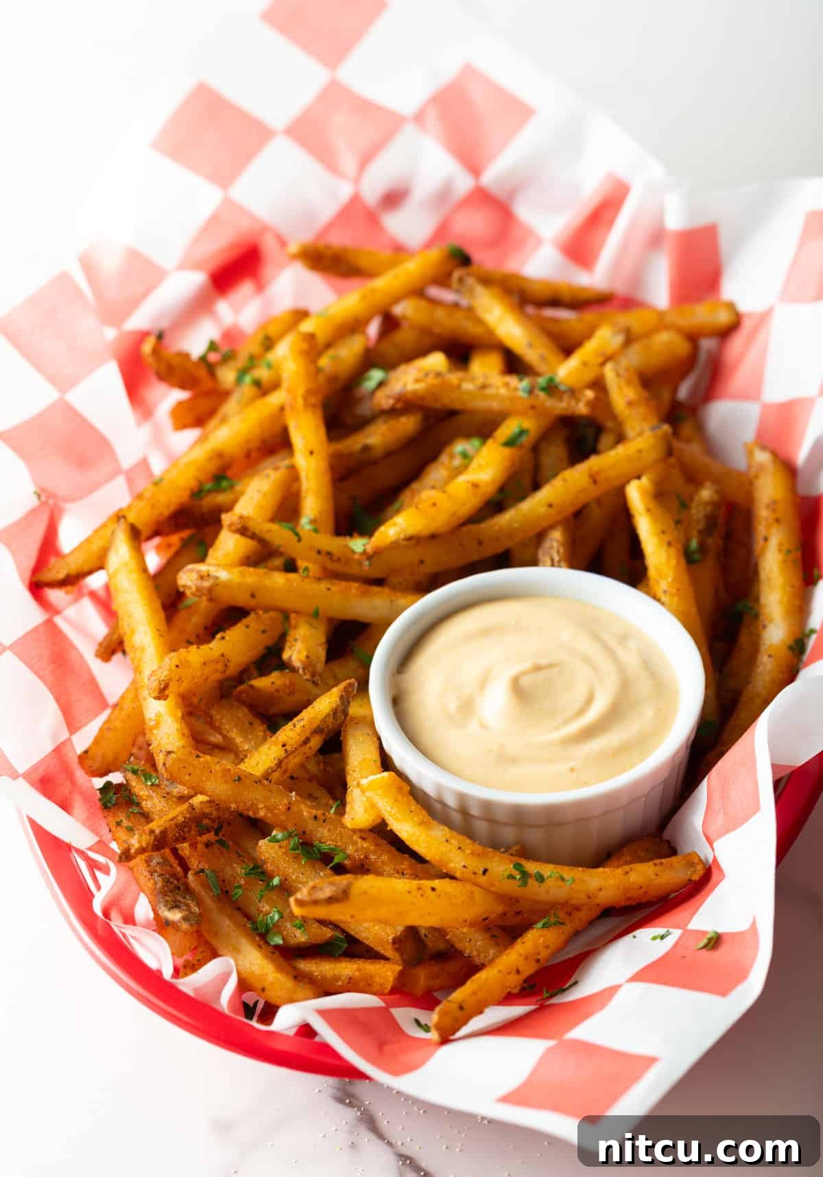 Next-Level Fry Sauces 3 A paper-lined basket of French fries surrounding a white ramekin filled with homemade French fry sauce.
