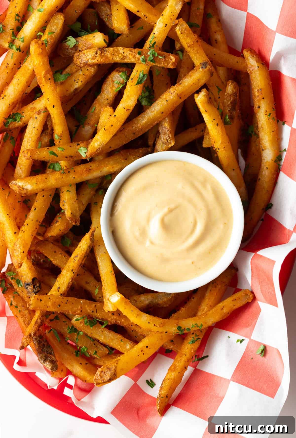Next-Level Fry Sauces 8 Overhead shot of a paper-lined basket of French fries surrounding a white ramekin filled with homemade French fry sauce.
