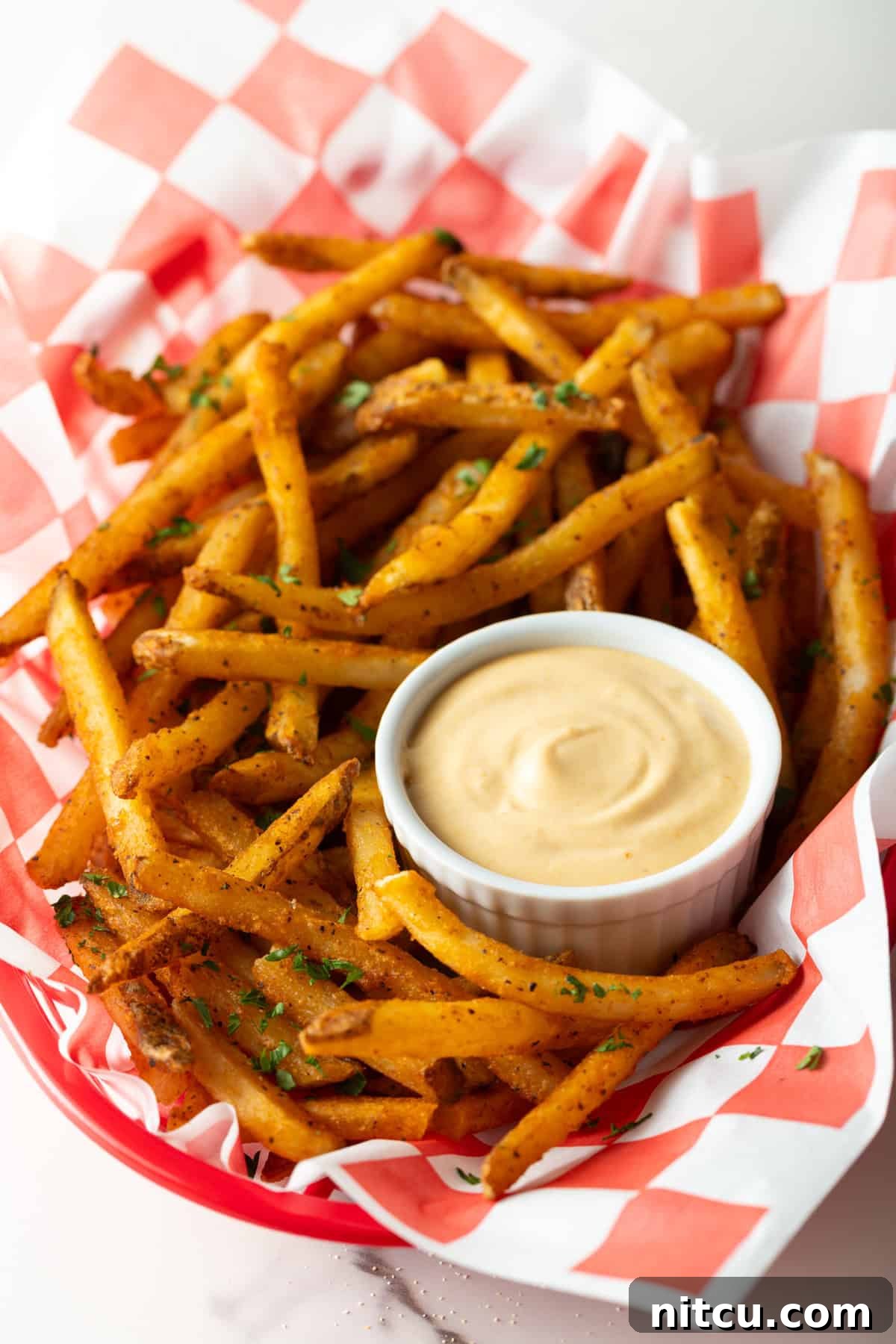Next-Level Fry Sauces 10 A paper-lined basket of French fries surrounding a white ramekin filled with creamy French fry sauce.