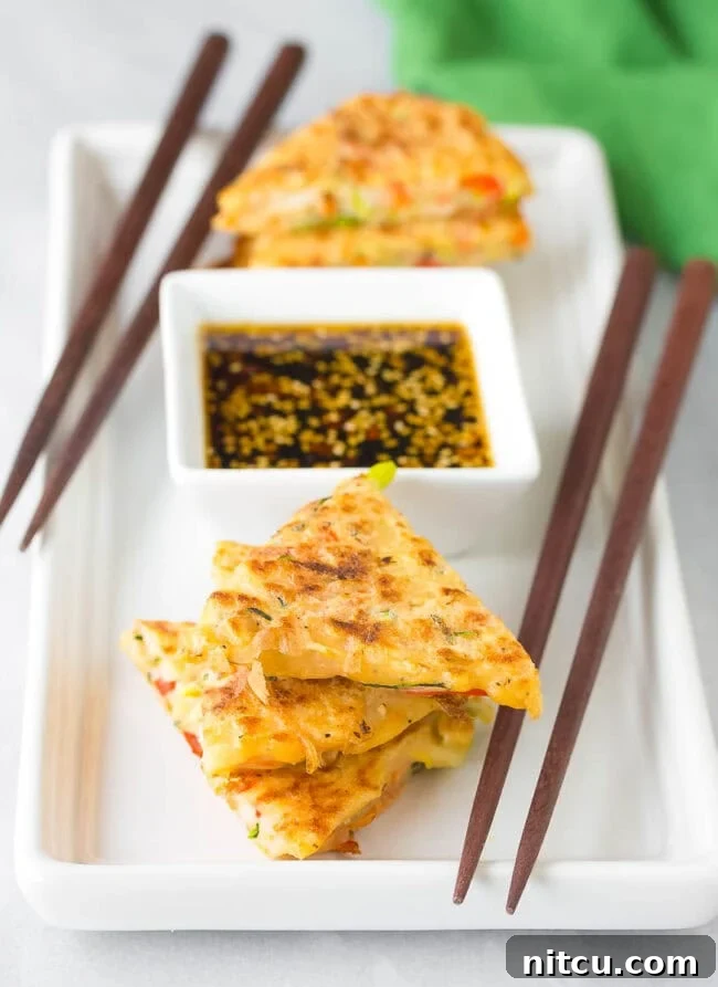 Authentic Korean Pancakes Pajeon Recipe Crispy Korean pancakes, Pajeon, cut into wedges and elegantly served on a plate next to a small bowl of spicy soy dipping sauce. The golden-brown edges promise a satisfying crunch.