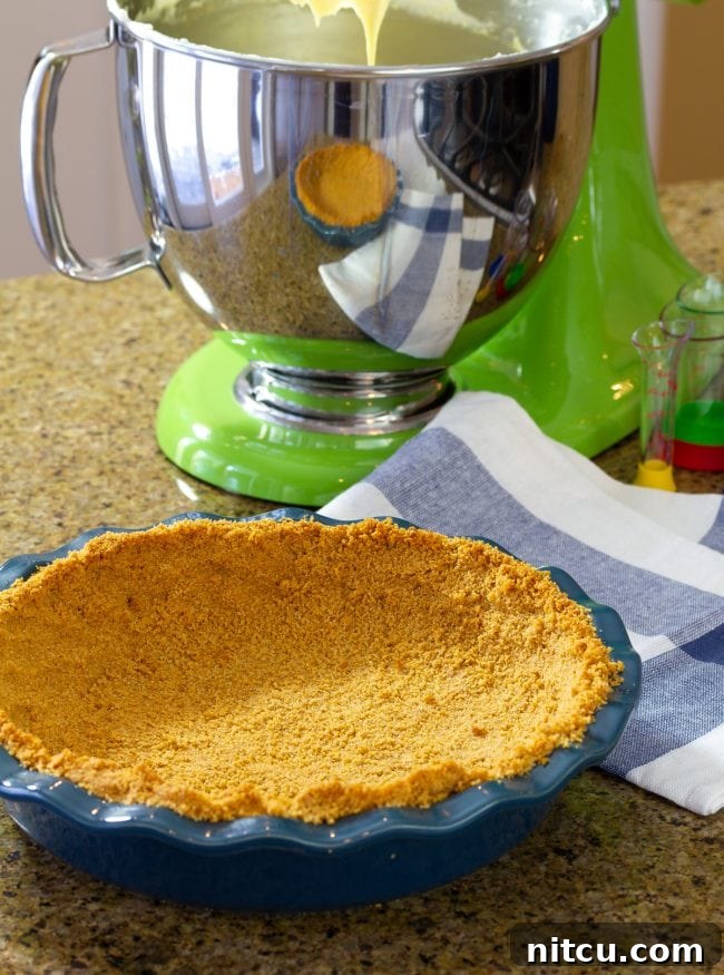 graham-crackers Graham Cracker Crust mixture in a pie dish, ready to be pressed, with a stand mixer in the background.
