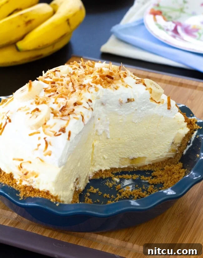 holiday-dessert The finished banana cream pie in a pie pan, showcasing the golden graham cracker crust, a towering whipped cream topping, and toasted coconut sprinkles.