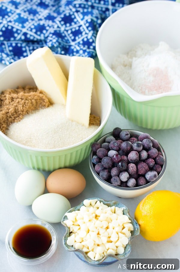 A collection of ingredients for Blueberry White Chocolate Blondies, including fresh blueberries, white chocolate chips, butter, sugars, and lemon.