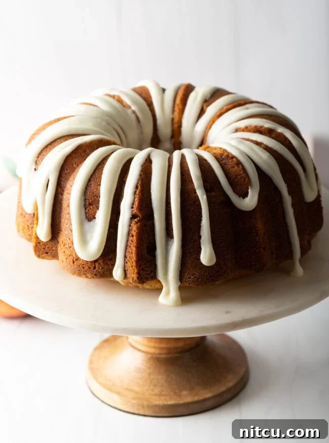 Luscious Peach Bundt Cake 2 Beautifully glazed peach bundt cake on a white cake stand, ready to be served.