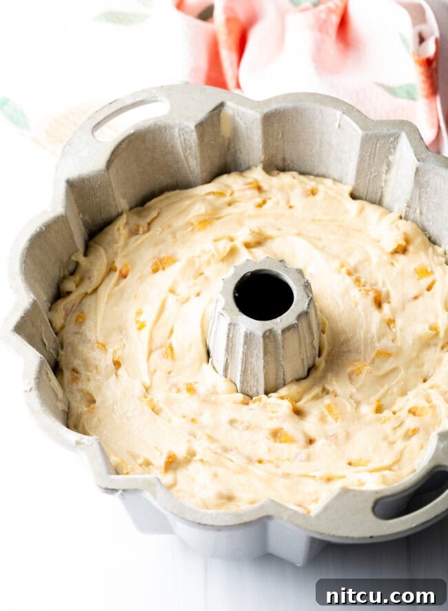 Luscious Peach Bundt Cake 6 Close-up of peach cake batter, layered with fresh peach pieces, inside a bundt pan before baking.