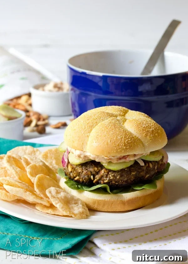 Signature Mediterranean Burger 10 A close-up of a beautifully assembled Mediterranean burger, garnished with fresh dill, served on a plate with chips.