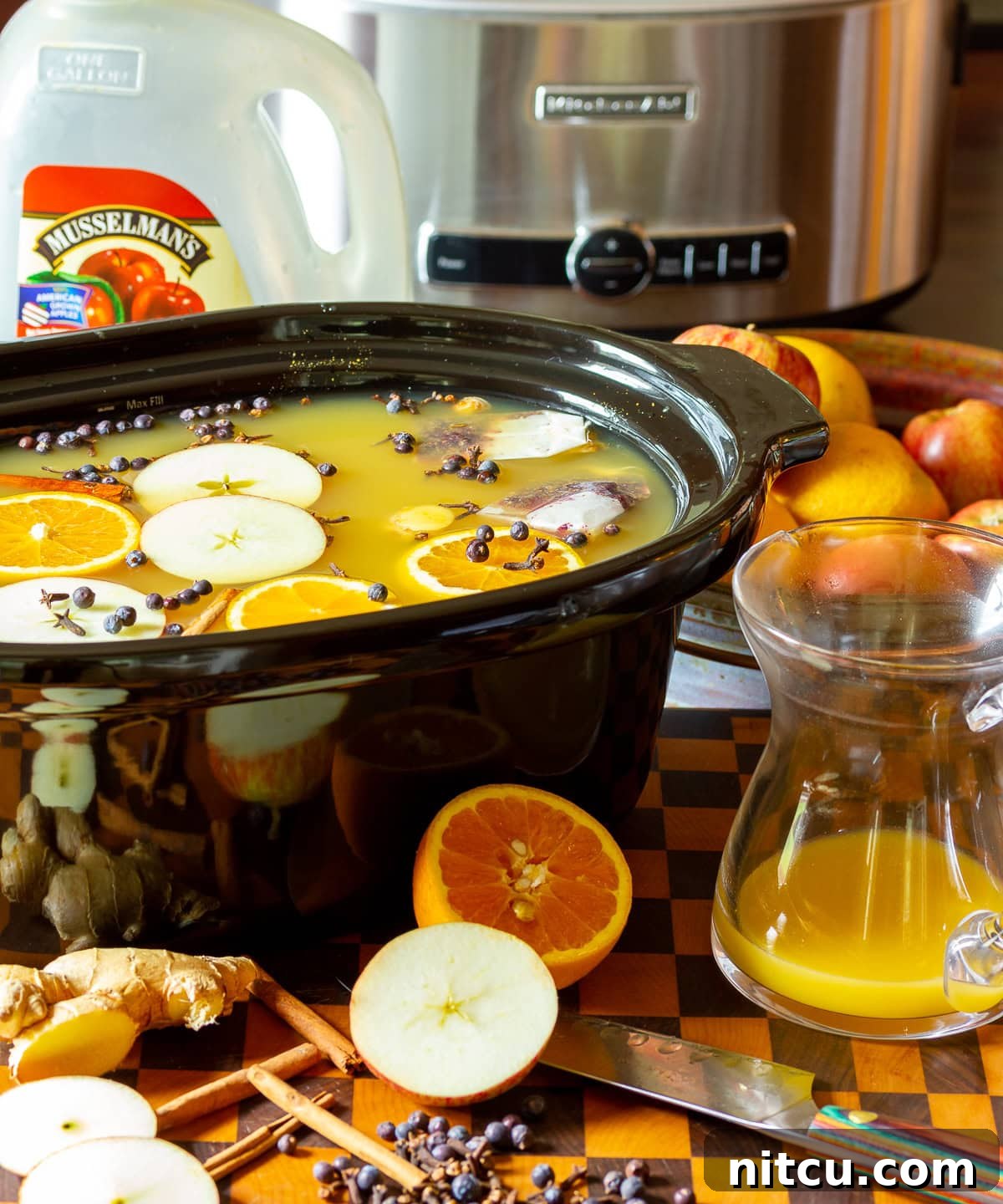 hot-apple-cider Apple cider wassail recipe in a crock pot with ingredients scattered in front.