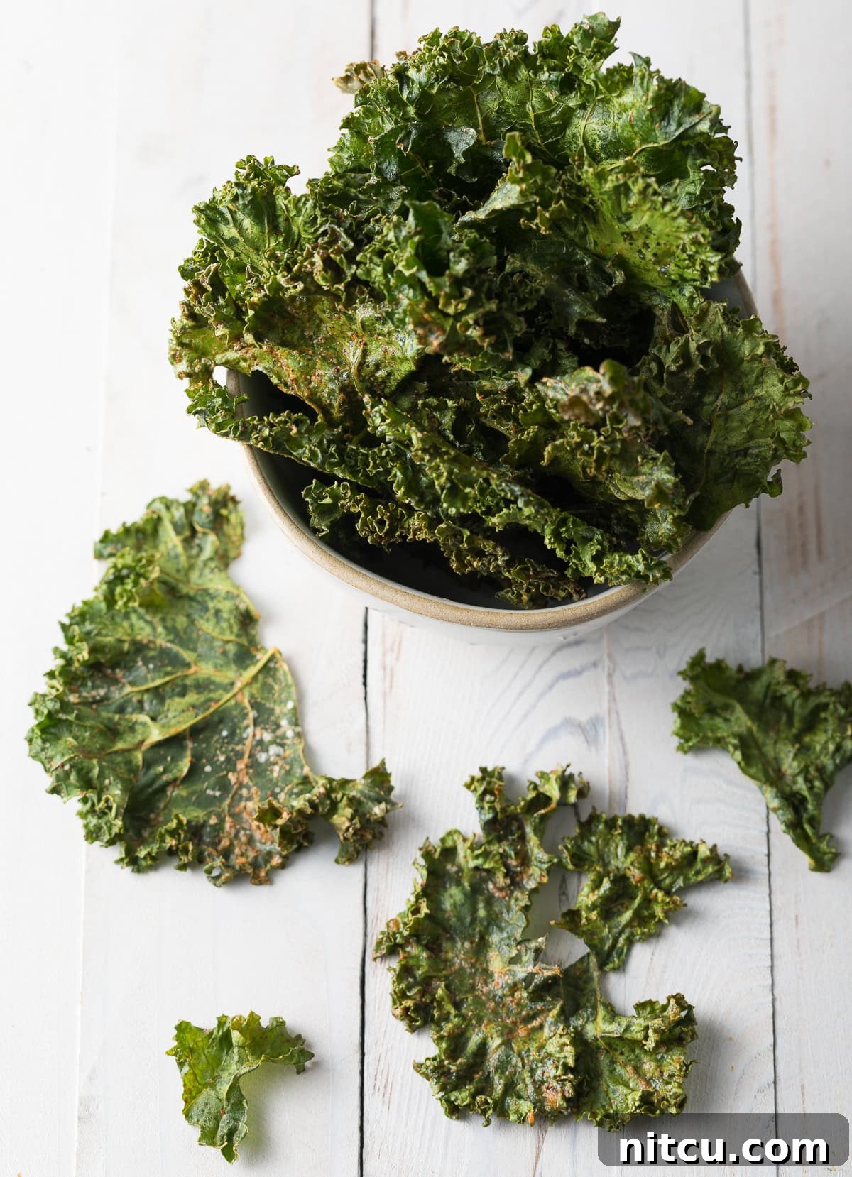 Effortless Crispy Kale Chips 10 Homemade kale chips in a bowl with a few scattered around.