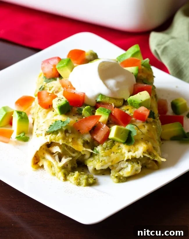 A delicious serving of sour cream Salsa Verde Chicken Enchiladas on a plate, garnished with fresh avocado slices and diced tomatoes.