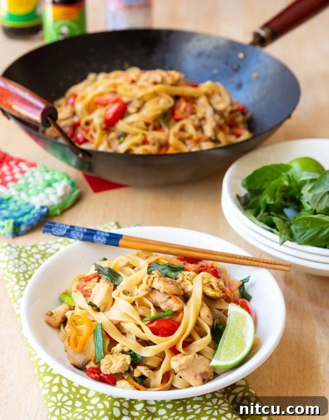 Addictive Pad Kee Mao Drunken Noodles Recipe 2 A bowl of delicious Pad Kee Mao (Drunken Noodles) garnished with fresh herbs and a lime wedge, ready to be enjoyed.
