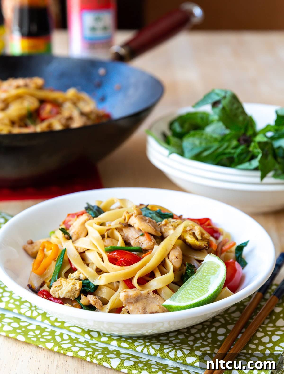 Addictive Pad Kee Mao Drunken Noodles Recipe 3 Close-up of freshly cooked Pad Kee Mao in a bowl, with a bright lime wedge and chopsticks ready for serving.
