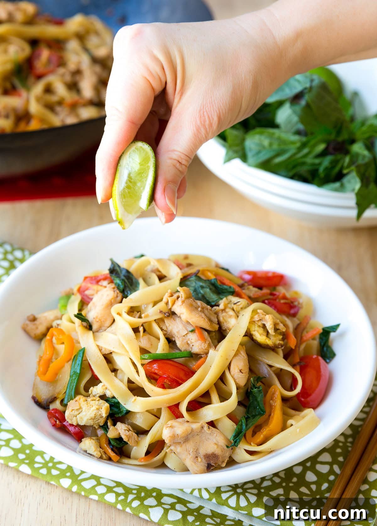 Addictive Pad Kee Mao Drunken Noodles Recipe 5 A hand squeezing a fresh lime wedge over a steaming bowl of Pad Kee Mao (Drunken Noodles), enhancing its fresh flavors.