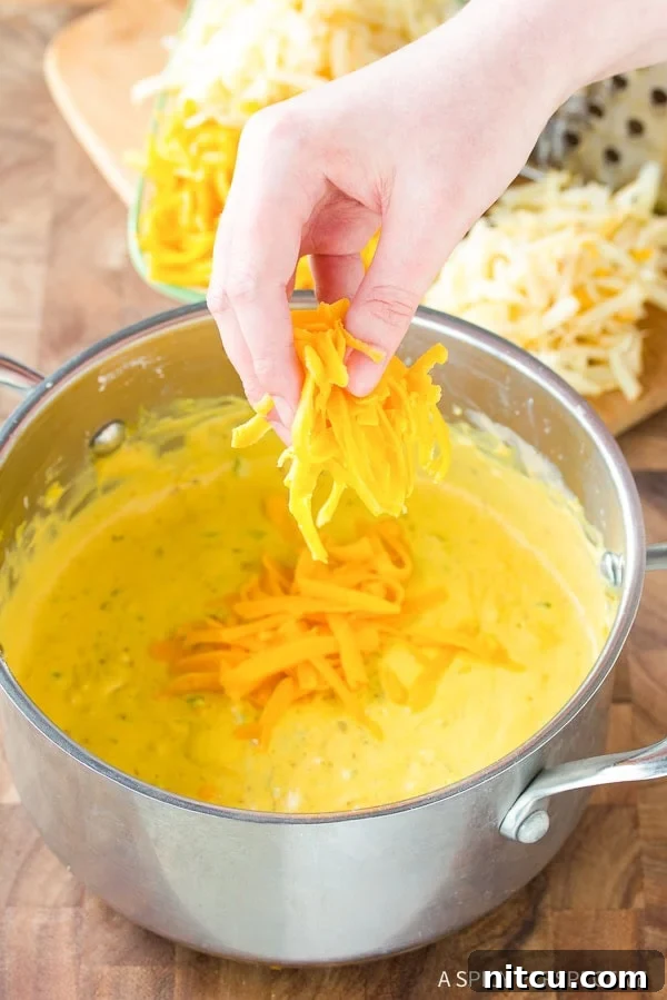 Creamy Homemade Queso 6 Hand gradually adding shredded cheddar cheese into the pot, stirring to melt evenly into the creamy sauce.