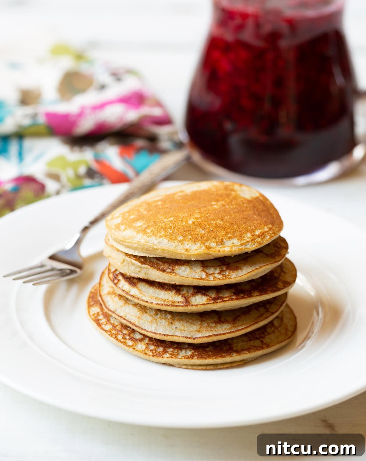 Fluffy Paleo Pancakes A beautifully stacked tower of five fluffy paleo pancakes, perfectly golden brown, resting on a pristine white plate, invitingly ready to be enjoyed.