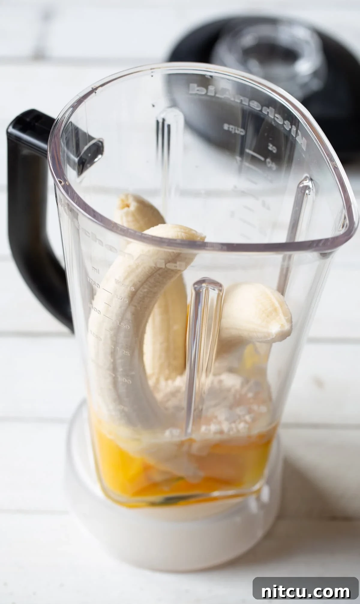 Blending Paleo Pancake Batter Three ripe bananas, a bowl of coconut flour, and eggs arranged inside a blender, ready to be combined into a smooth paleo pancake batter.