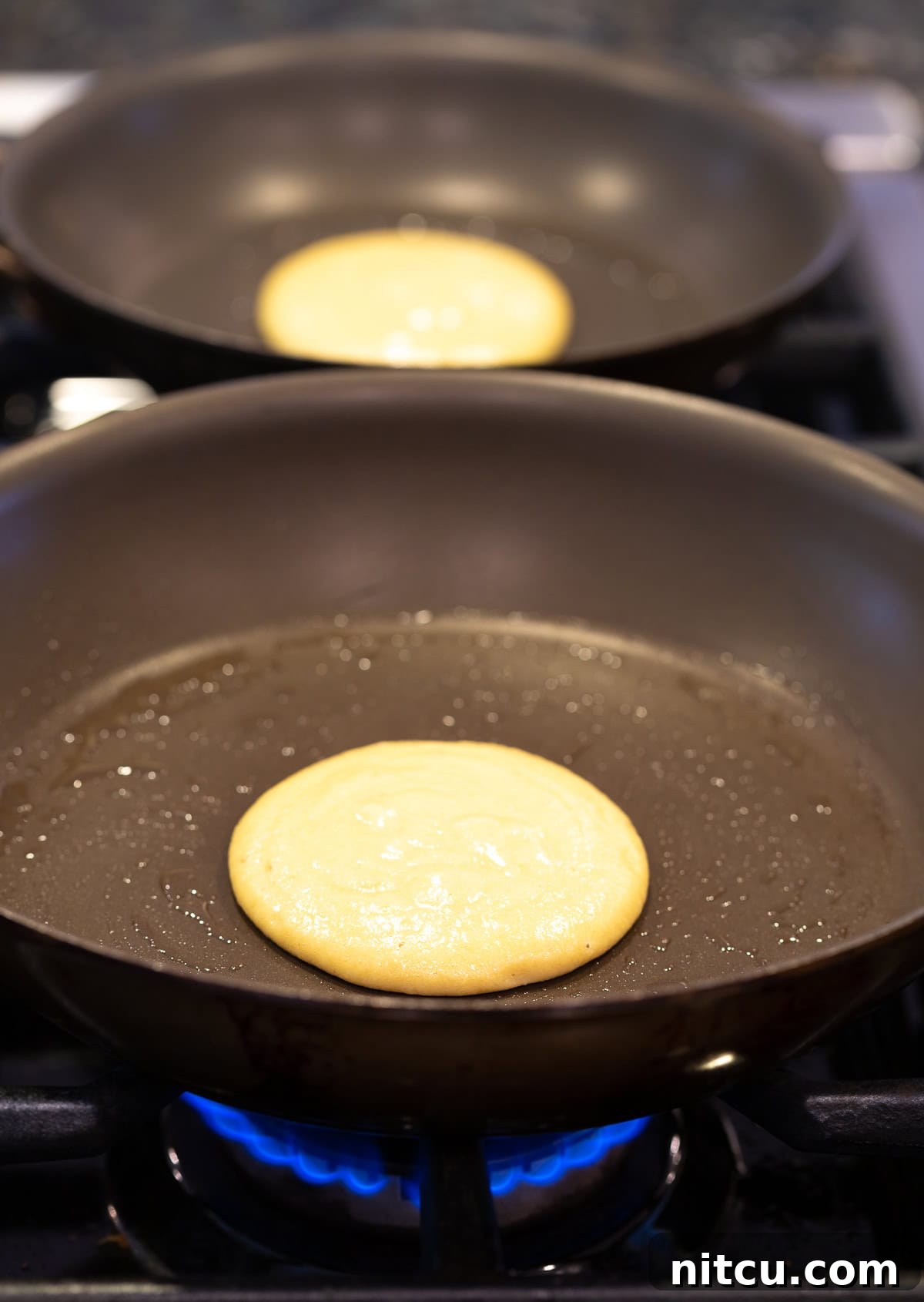 Cooking Paleo Pancakes A golden-brown coconut flour pancake being cooked to perfection in a hot non-stick skillet on a stovetop, capturing the cooking process.