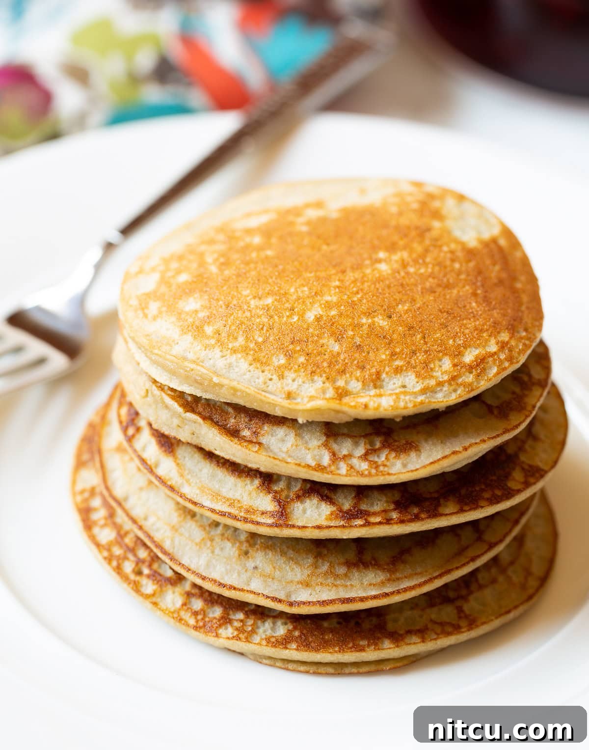 Paleo Pancake Presentation A stack of five golden-brown paleo pancakes on a white plate, subtly garnished, showcasing their inviting texture.
