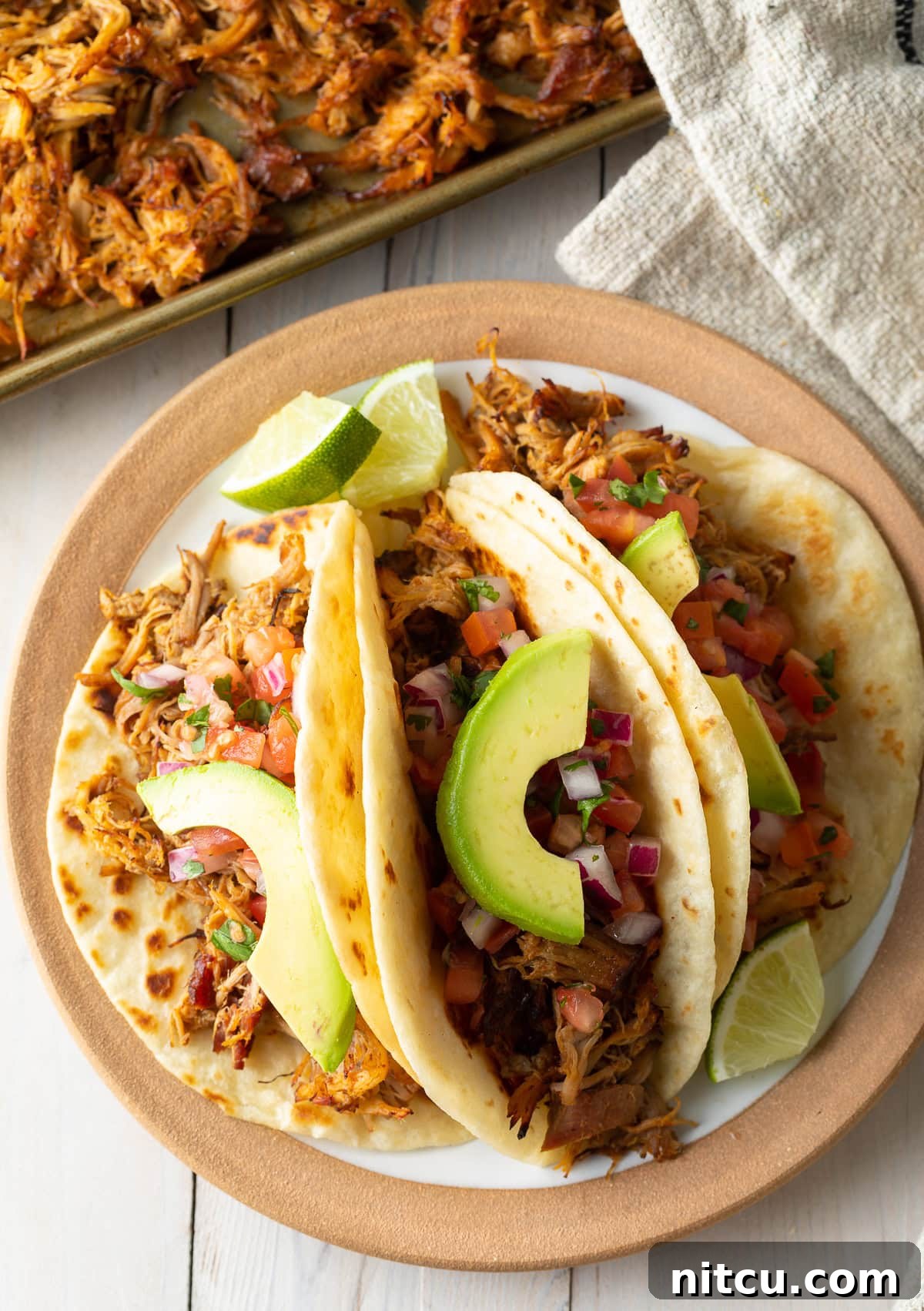 Carnitas-Recipe-Slow-Cooker Overhead shot of three perfectly assembled carnitas tacos with avocado slices on a plate, ready to be enjoyed.