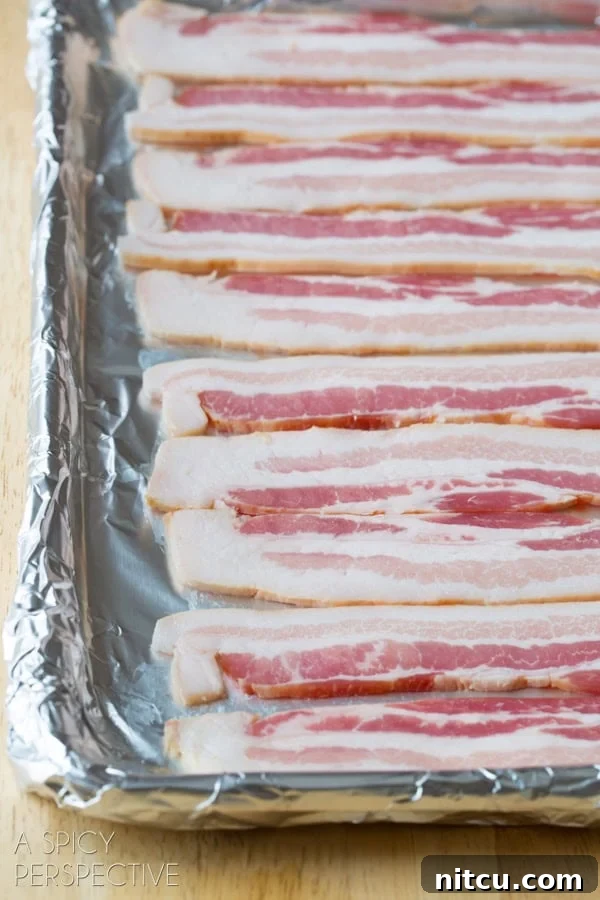 Closeup of oven-baked bacon strips on a metal cooling rack set inside a rimmed baking sheet, showing the even crispiness and rendered fat collected below. #ASpicyPerspective #BaconinTheOven #Bacon #Oven #BakingBacon #HowtoCookBaconinTheOven #CookingBaconintheOven #HowtoBakeBacon #OvenBakedBacon #CrispyBacon #EasyBacon