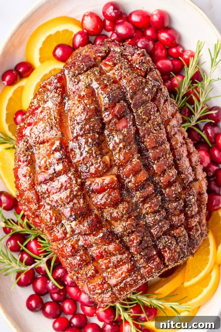 Caramelized Brown Sugar Glazed Ham 2 Overhead shot of perfectly baked brown sugar glazed ham on a festive serving platter, garnished with fresh cranberries, orange slices, and aromatic rosemary, ready to be carved for a holiday feast.