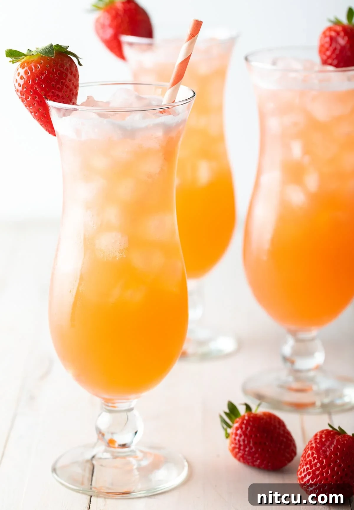 Crafting Refreshing Agua Fresca 3 3 tall cocktail beverage glasses filled with strawberry pineapple agua fresca. Each glass is garnished with a strawberry on the rim and and orange and white striped paper straw.