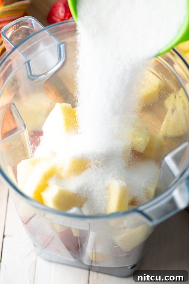 Crafting Refreshing Agua Fresca 5 Pouring sugar into a blender pitcher with chunks of pineapple and strawberries.